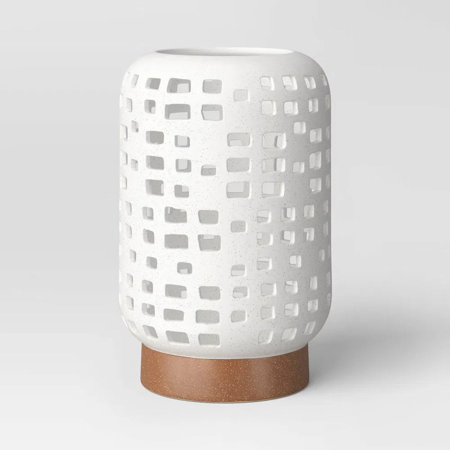 Large cutout ceramic lantern candle holder in speckled white on a brown foot, on a plain light grey background
