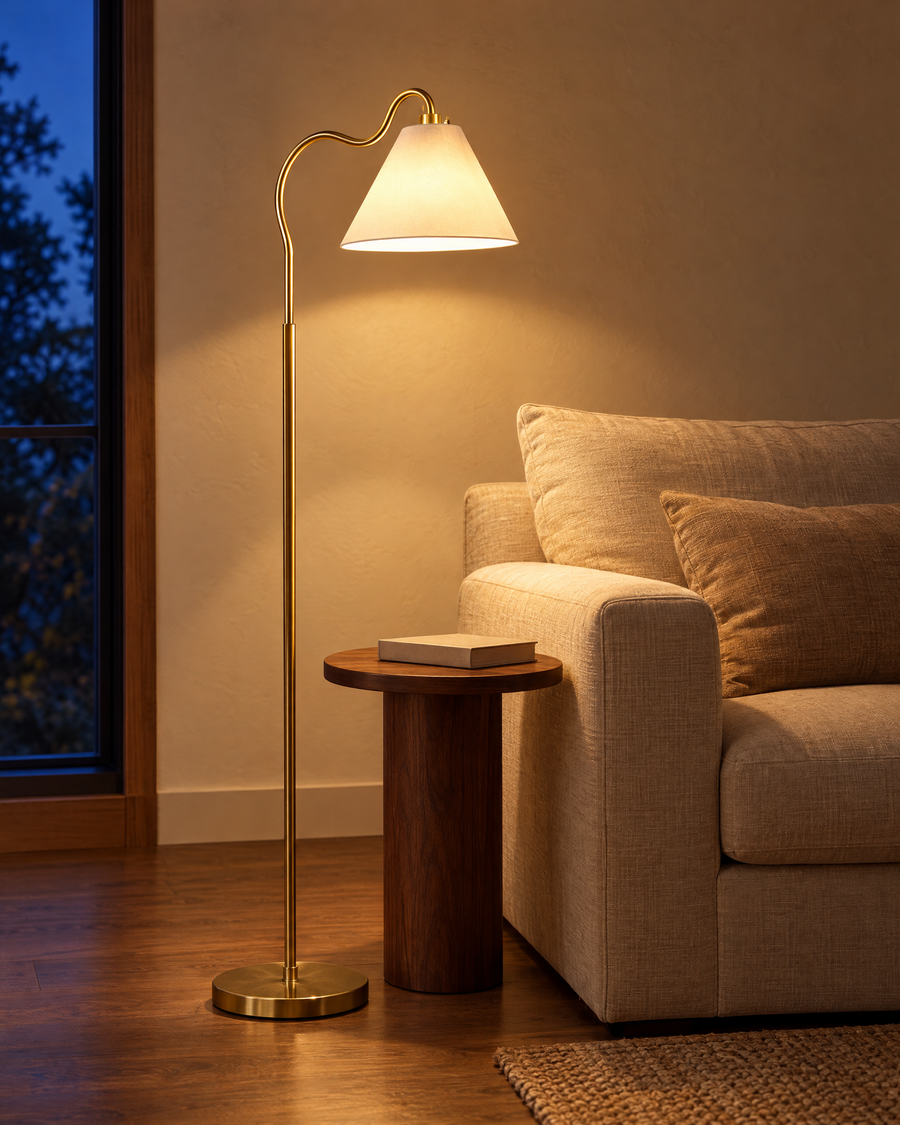 Curved Brass Floor Lamp, Round Base, Cone Shade, Gold & White Finish lit in a living room reading corner at dusk