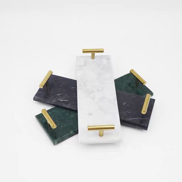 Marble vanity trays with brass-tone T-bar handles in white, charcoal and emerald, overlapping on a plain white background