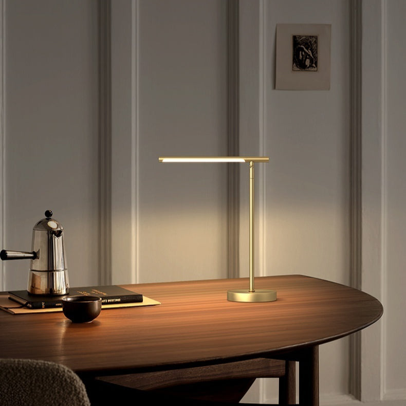 Brushed brass desk lamp with a level light bar, lit on a walnut desk against a pale paneled wall