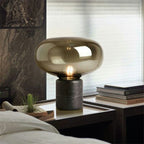 Amber glass mushroom table lamp lit on a bedside table beside a stack of books