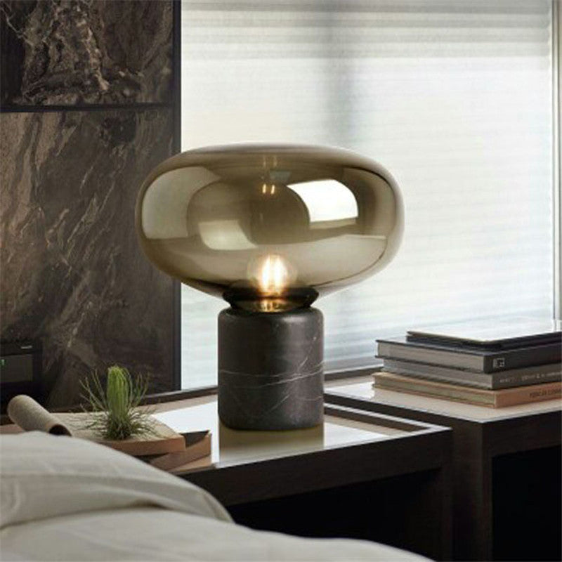 Amber glass mushroom table lamp lit on a bedside table beside a stack of books
