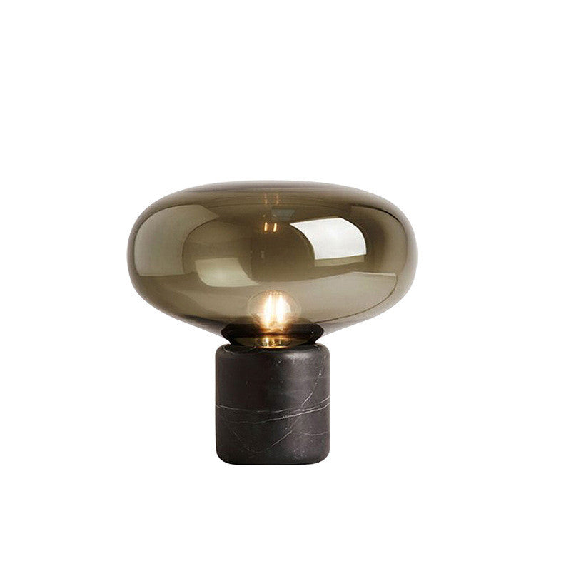 Amber glass mushroom table lamp with veined black base, lit, on a plain white background