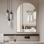 Arched brushed gold mirror hung above a bathroom vanity between pendant lights