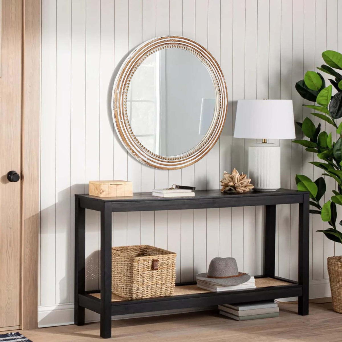 Beaded round wall mirror above a black entry console with a white table lamp and basket