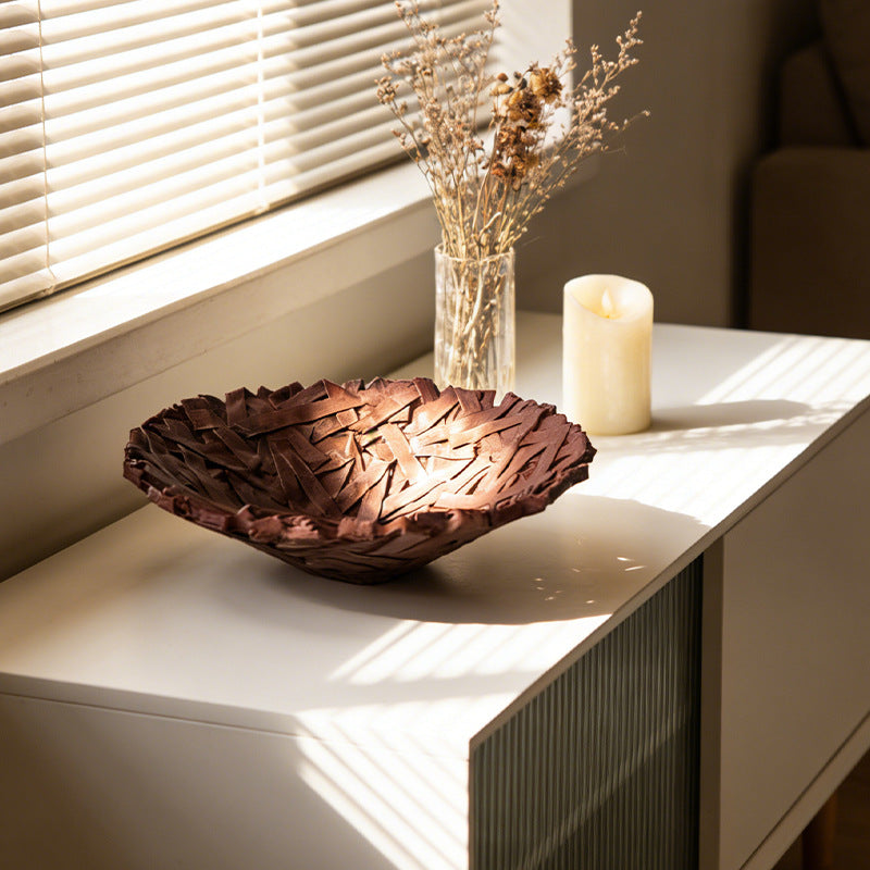 Deep brown nest-texture resin bowl on a white sideboard by a window with a candle