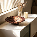 Deep brown nest-texture resin bowl on a white sideboard by a window with a candle