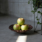 Bird's nest resin bowl holding three green apples on a concrete floor