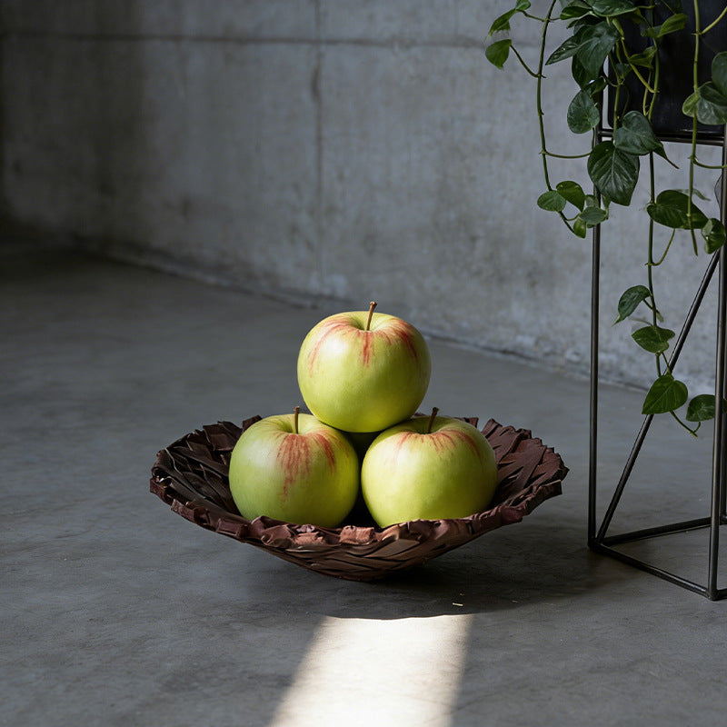 Bird's nest resin bowl holding three green apples on a concrete floor