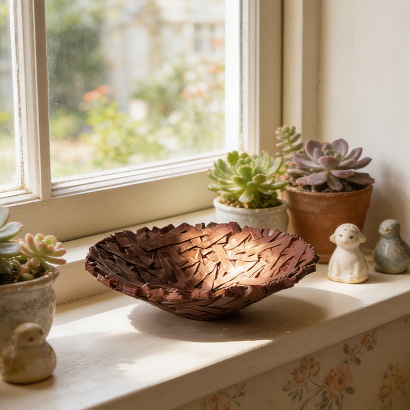 Deep brown bird's nest bowl on a sunny windowsill beside succulents and small figurines