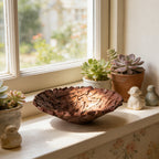 Deep brown bird's nest bowl on a sunny windowsill beside succulents and small figurines