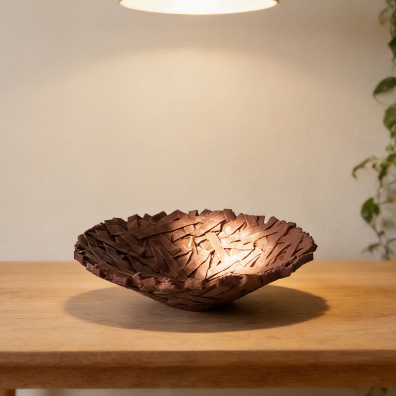 Bird's nest resin fruit bowl in deep brown on a wooden table under a pendant light