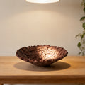 Bird's nest resin fruit bowl in deep brown on a wooden table under a pendant light