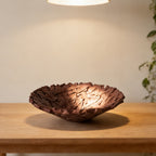Bird's nest resin fruit bowl in deep brown on a wooden table under a pendant light