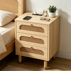 Cane three-drawer nightstand beside a bed with a clock, glasses and a charging phone on top
