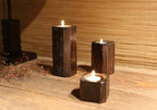 Charred wood tealight holders lit beside dried red berries on a wooden table