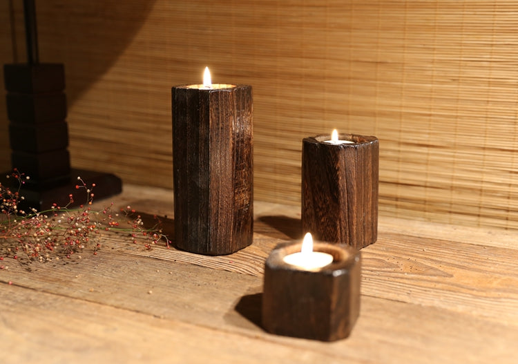 Charred wood tealight holders lit beside dried red berries on a wooden table