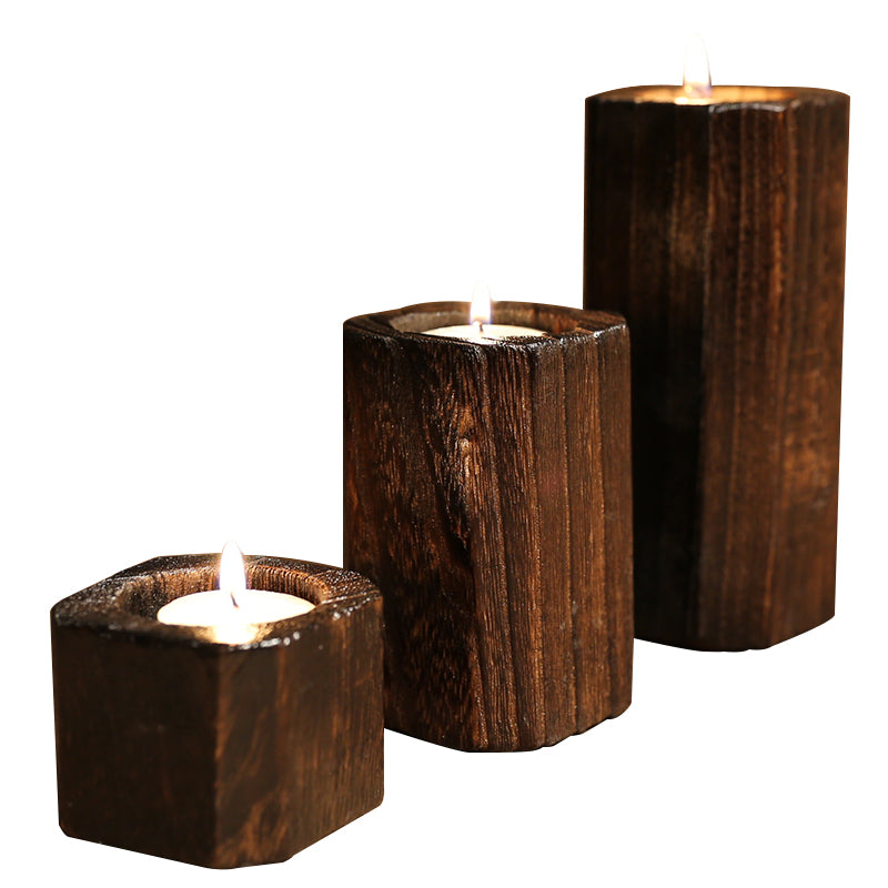 Charred wood tealight holders in three heights, lit, on a plain white background