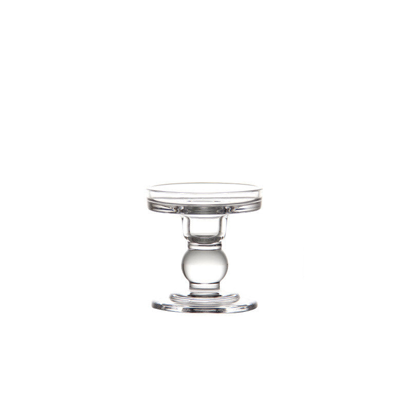 Short clear glass candle holder with a ball stem on a plain white background