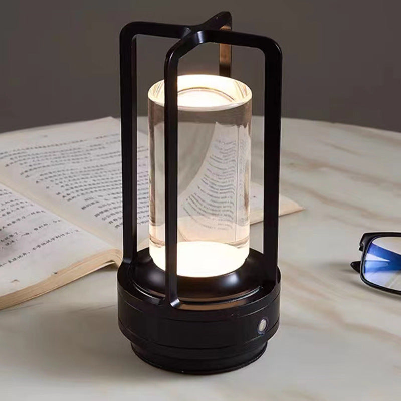 Black cordless lantern table lamp, lit on a marble table beside an open book and glasses