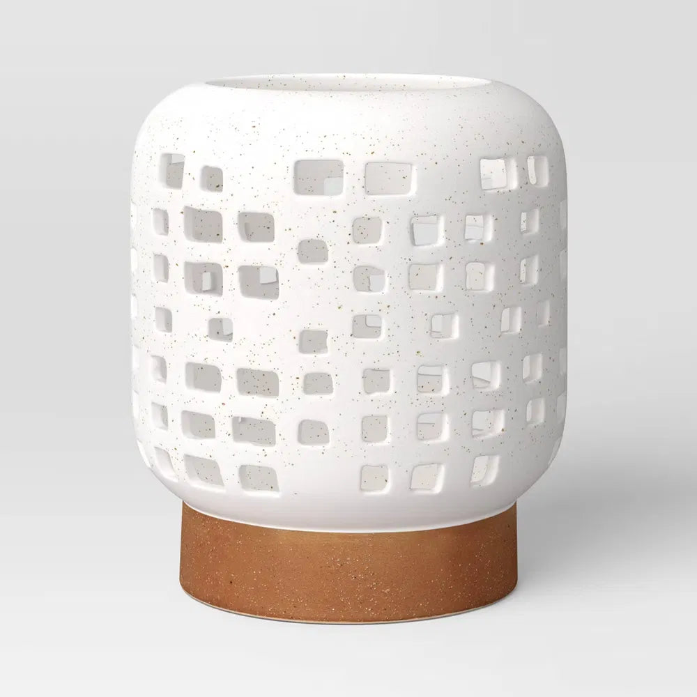 Small cutout ceramic lantern candle holder in speckled white on a brown foot, on a plain light grey background