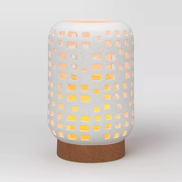 Large ceramic lantern candle holder glowing through its square cutouts, on a plain grey background