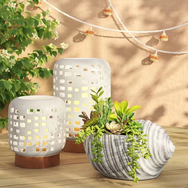 Small and Large cutout ceramic lanterns lit on a wooden patio table beside a shell planter