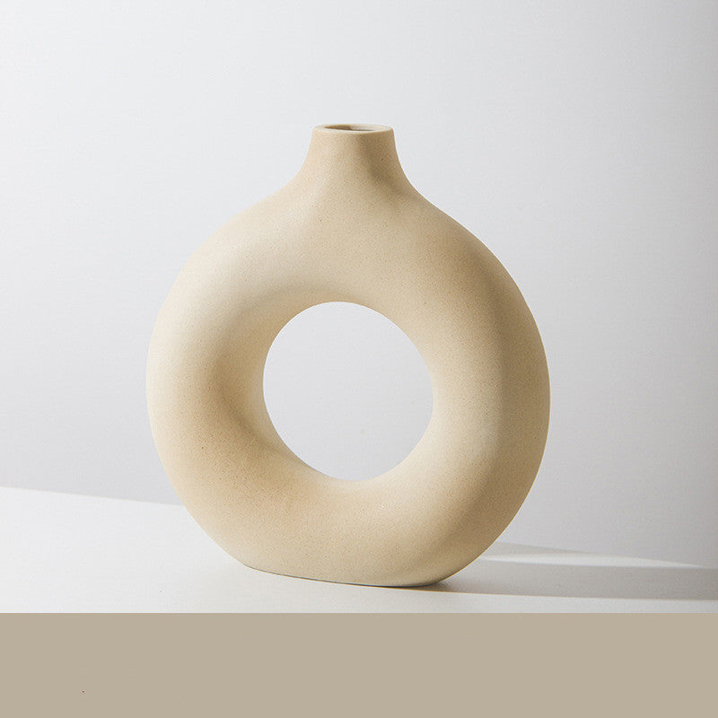 Donut ring porcelain bud vase in sand, speckled matte finish, on a white tabletop against a pale wall