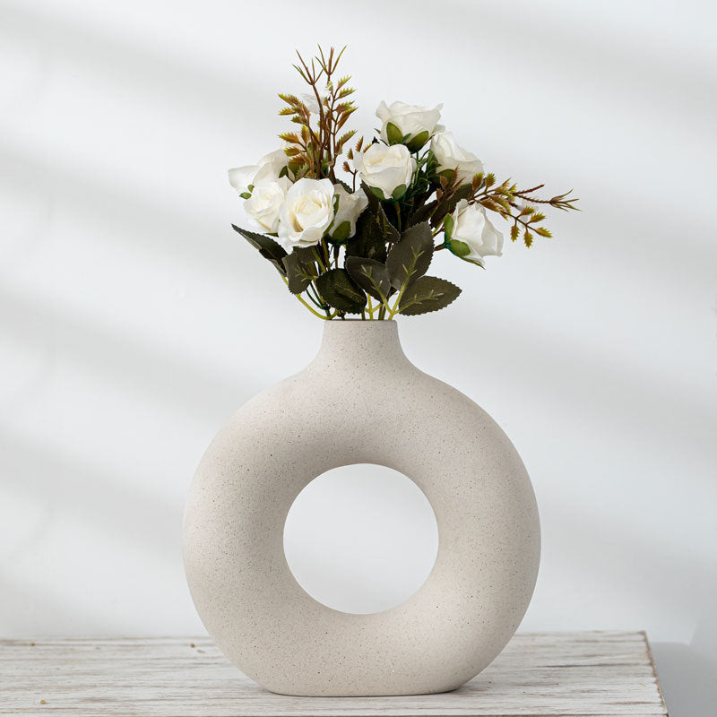 Donut ring porcelain bud vase in ivory holding white roses on a whitewashed wood shelf