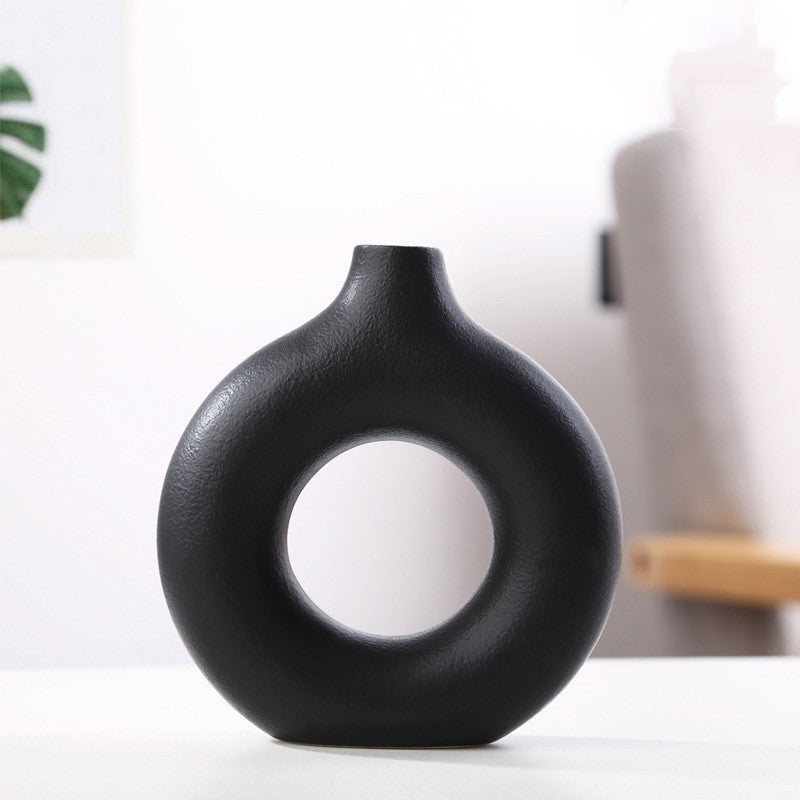Donut ring porcelain bud vase in matte black, small size, on a white tabletop in a bright room