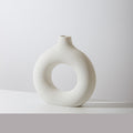 Donut ring porcelain bud vase in ivory, speckled matte finish, on a white tabletop against a pale grey wall