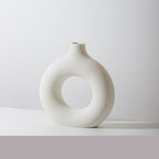 Donut ring porcelain bud vase in ivory, speckled matte finish, on a white tabletop against a pale grey wall