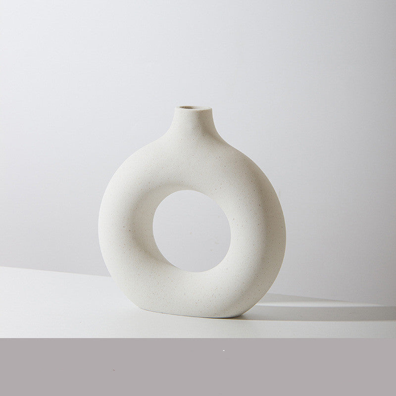 Donut ring porcelain bud vase in ivory, speckled matte finish, on a white tabletop against a pale grey wall