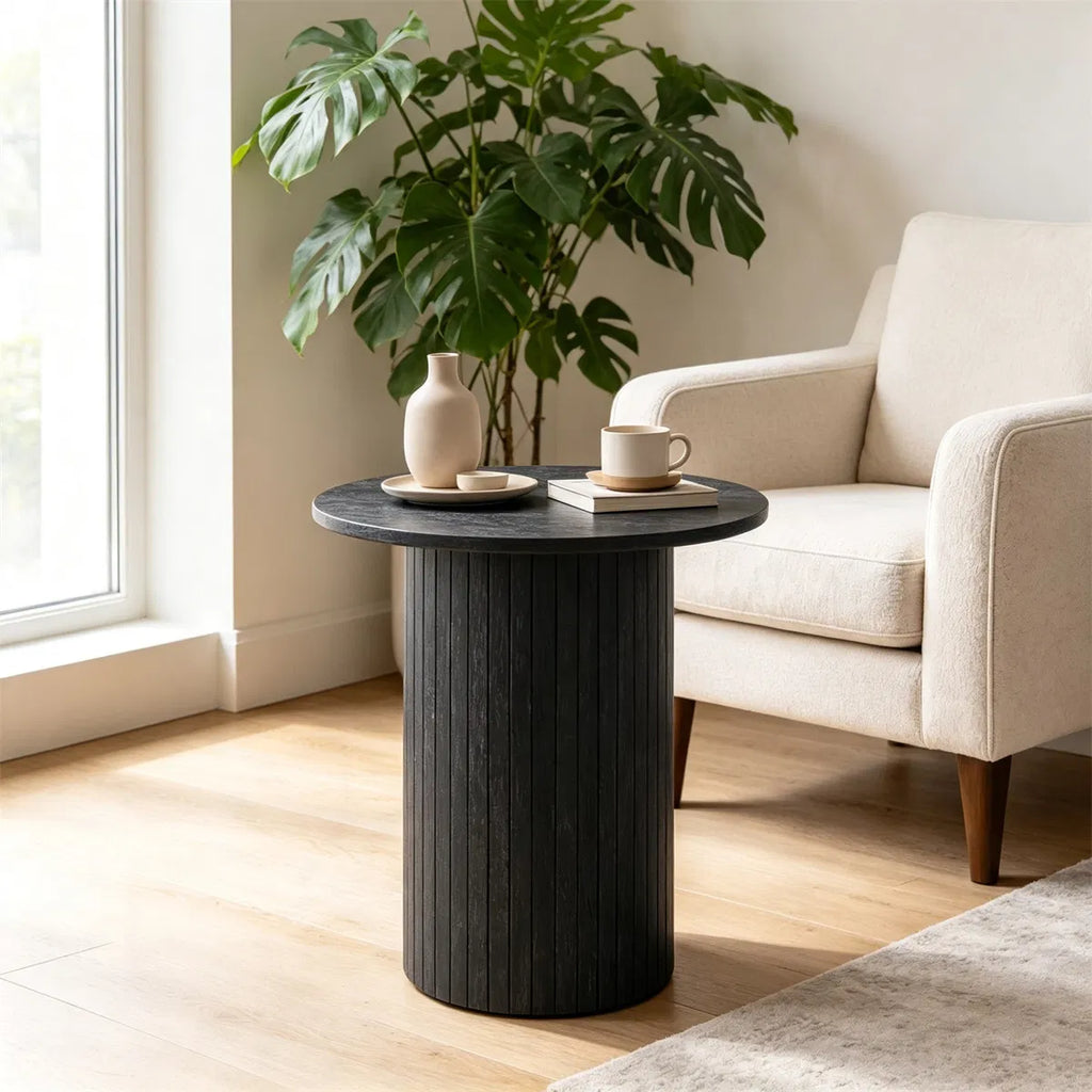 Black fluted pedestal side table beside a cream armchair in a sunlit living room