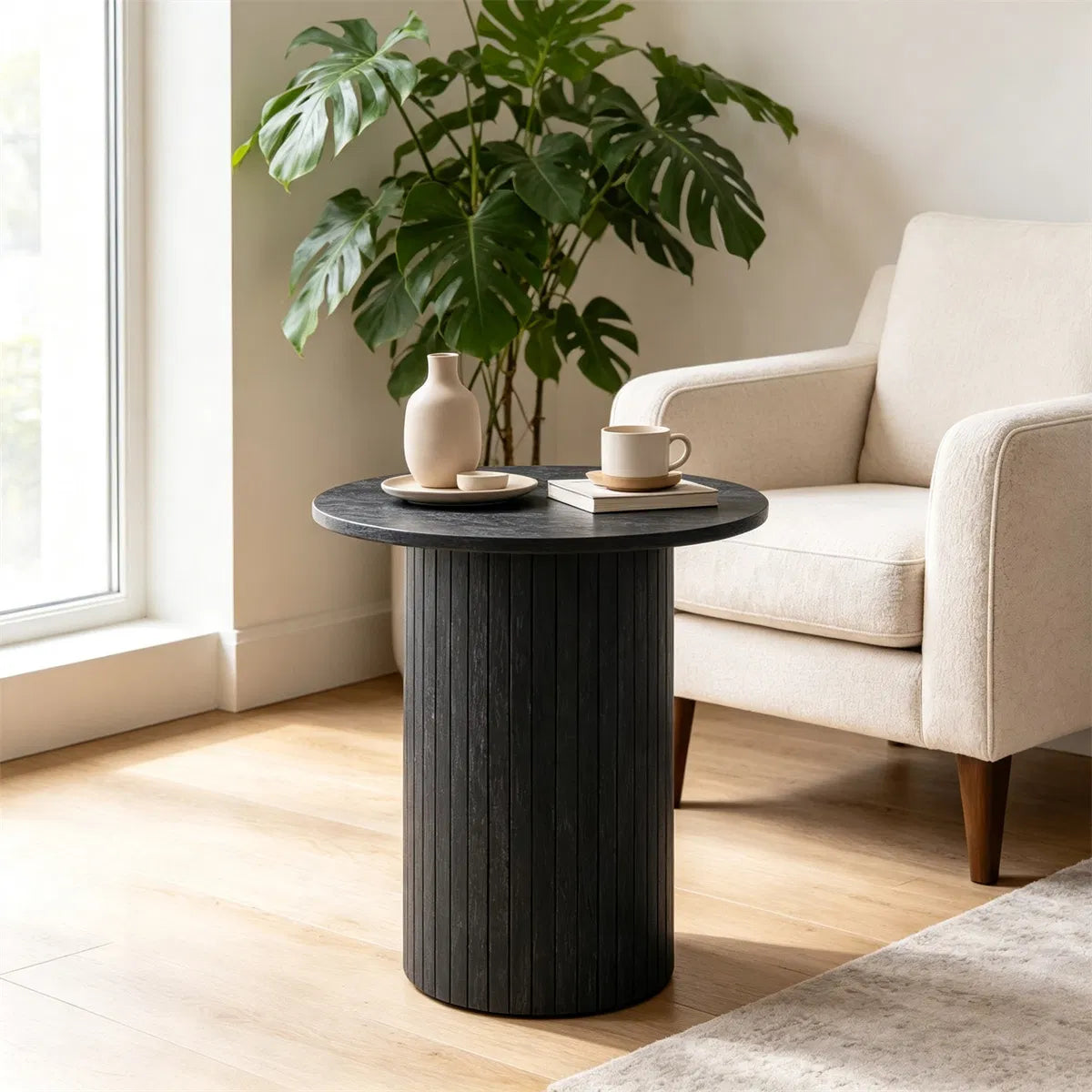 Black fluted pedestal side table beside a cream armchair in a sunlit living room