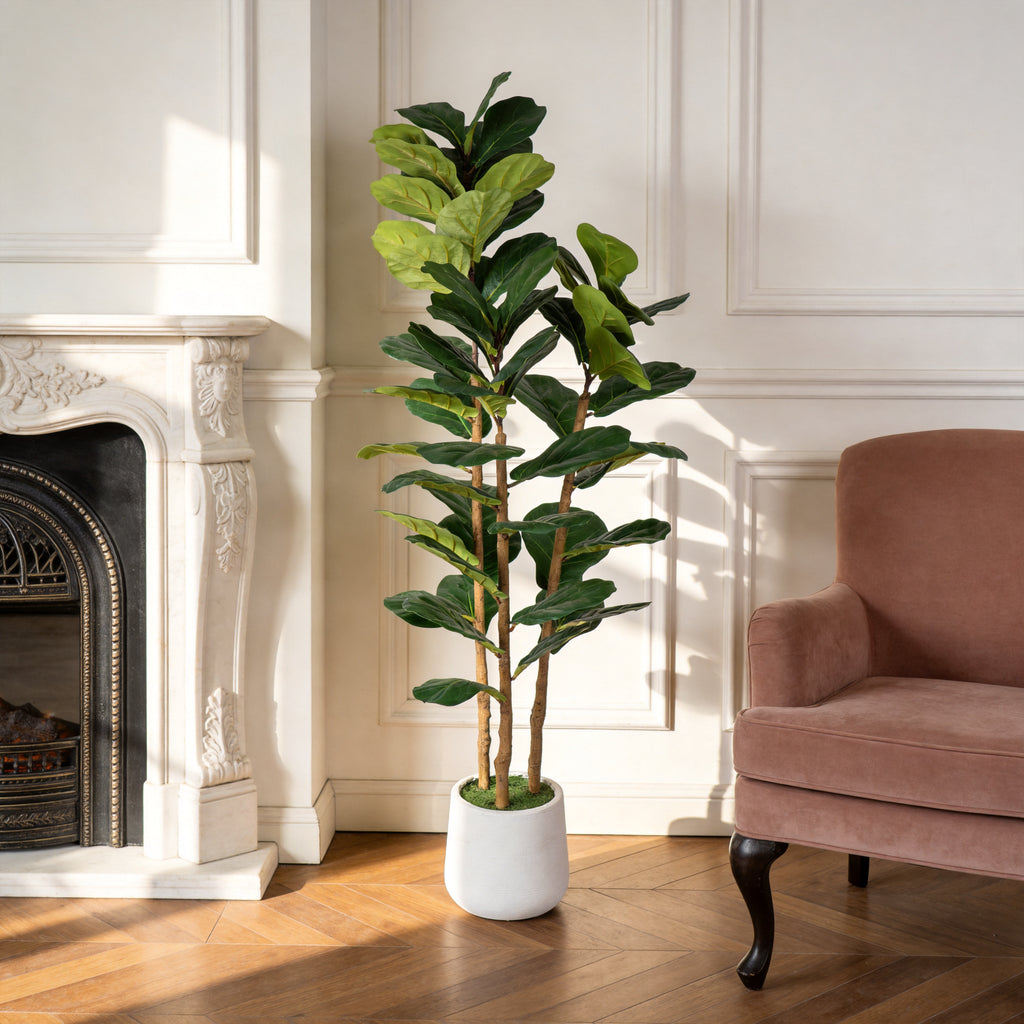 Faux fiddle leaf fig in a white pot beside a carved fireplace and a rose velvet armchair