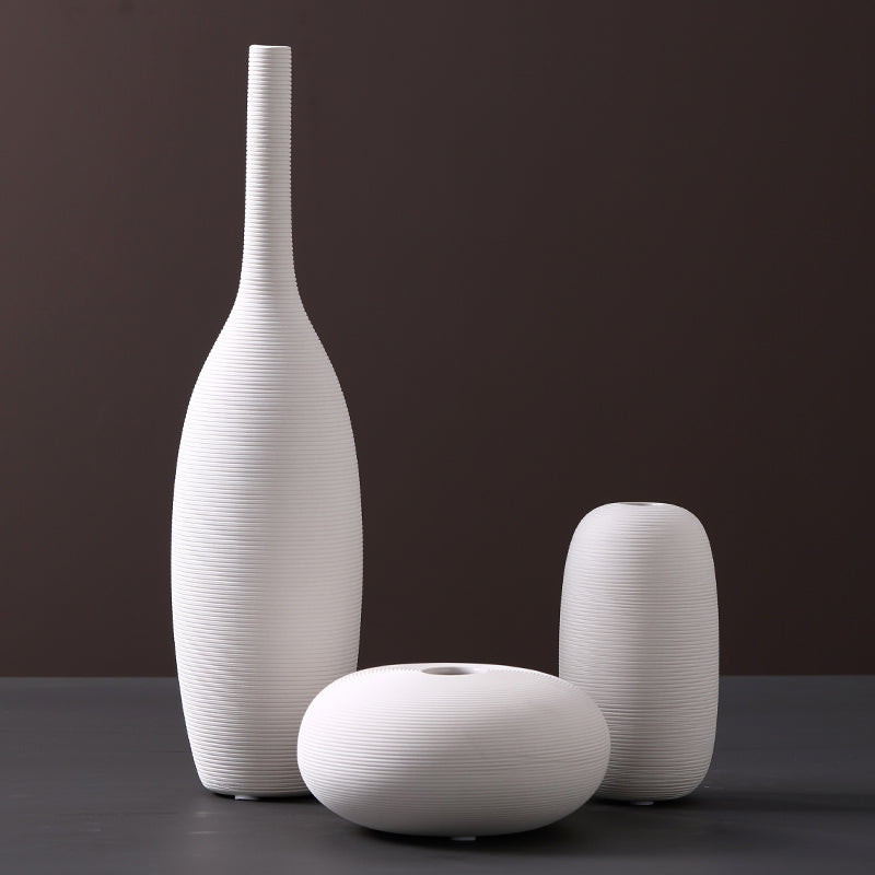 Fine-ribbed white ceramic vases, tall bottle, pebble and small capsule, on a dark grey studio backdrop