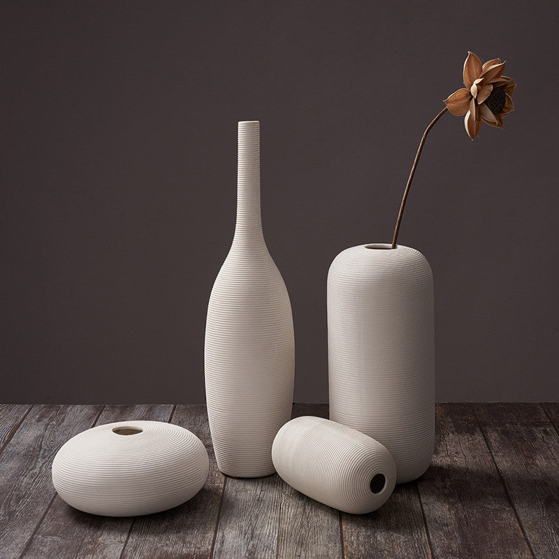 Fine-ribbed white ceramic vases, set of four with the tall bottle, on weathered wood under warm light