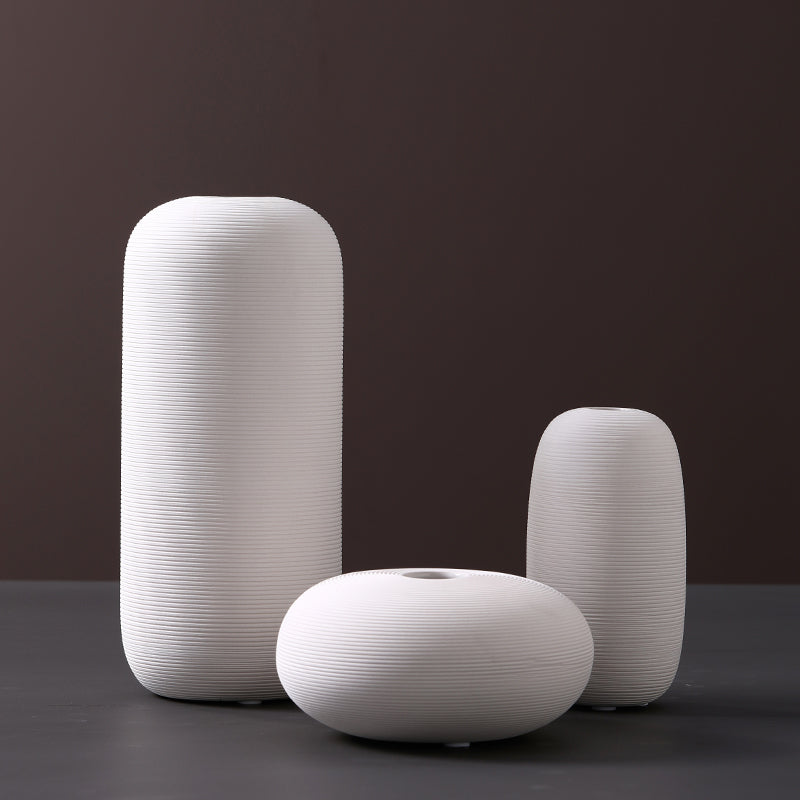 Fine-ribbed white ceramic vases, tall capsule, pebble and small capsule, on a dark grey studio backdrop