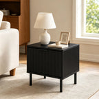 Fluted black nightstand beside an armchair with a lamp and picture frame