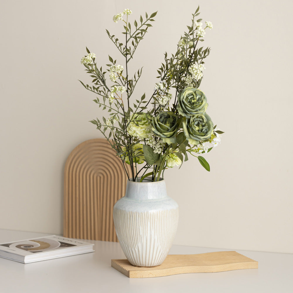 Fluted ceramic vase with pale blue shoulder holding faux green roses and white blossom stems on a console