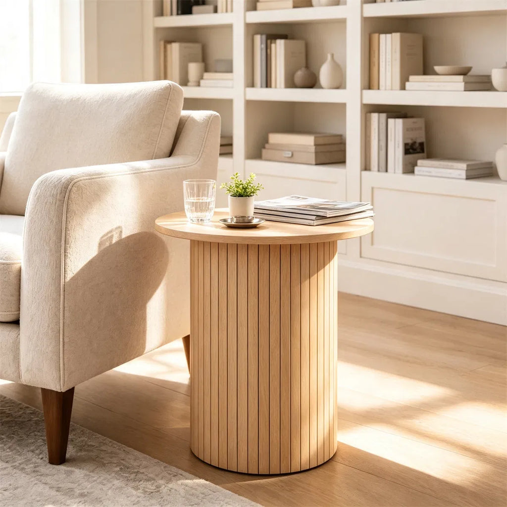Natural fluted pedestal side table next to a cream armchair in front of white shelves