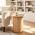 Natural fluted pedestal side table next to a cream armchair in front of white shelves