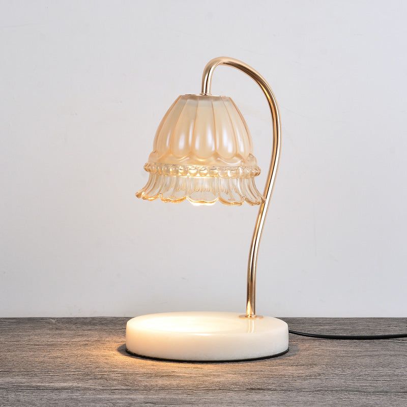 Candle warmer lamp lit on a grey wood tabletop, its glow pooling on the white marble base
