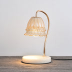 Candle warmer lamp lit on a grey wood tabletop, its glow pooling on the white marble base