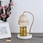 Candle warmer lamp unlit, a gold jar candle on its marble base, beside roses and a white frame