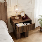 Fluted pedestal nightstand with the drawer open beside a bed, holding a notebook and headphones