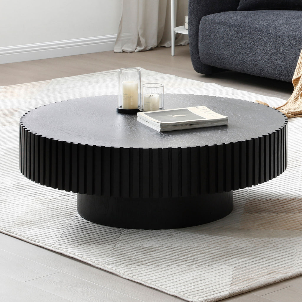 Black fluted round coffee table on a striped cream rug in a bright living room