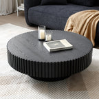 Fluted drum coffee table in matte black seen from above, with candle holders and a book on a cream rug