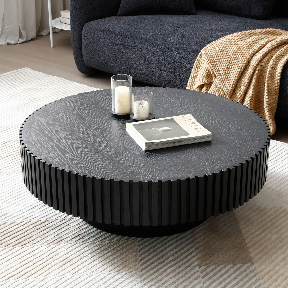 Fluted drum coffee table in matte black seen from above, with candle holders and a book on a cream rug